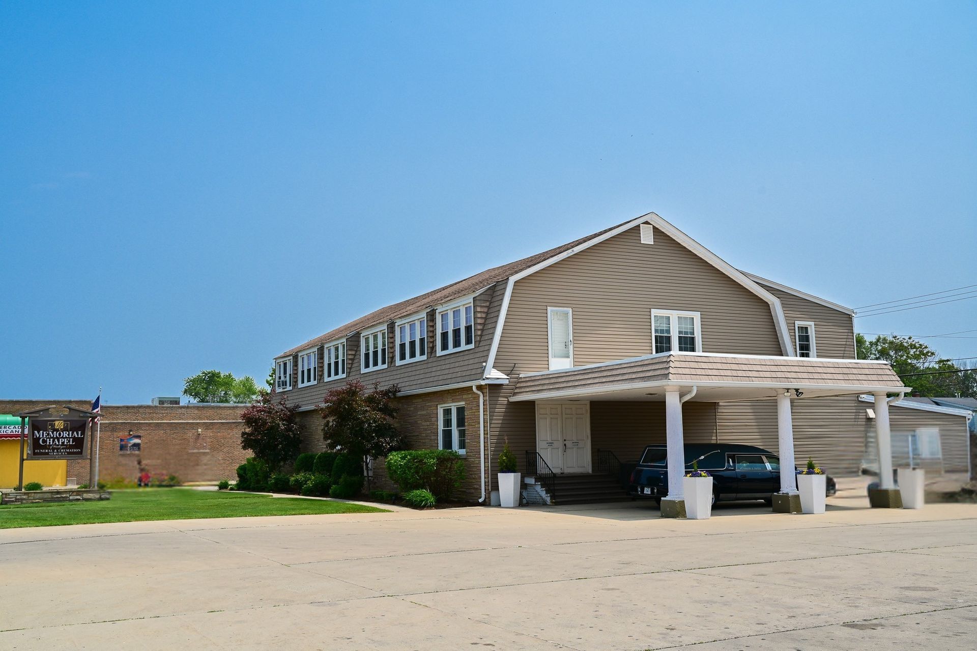 Two-story tan building with white carport and parked cars under a blue sky