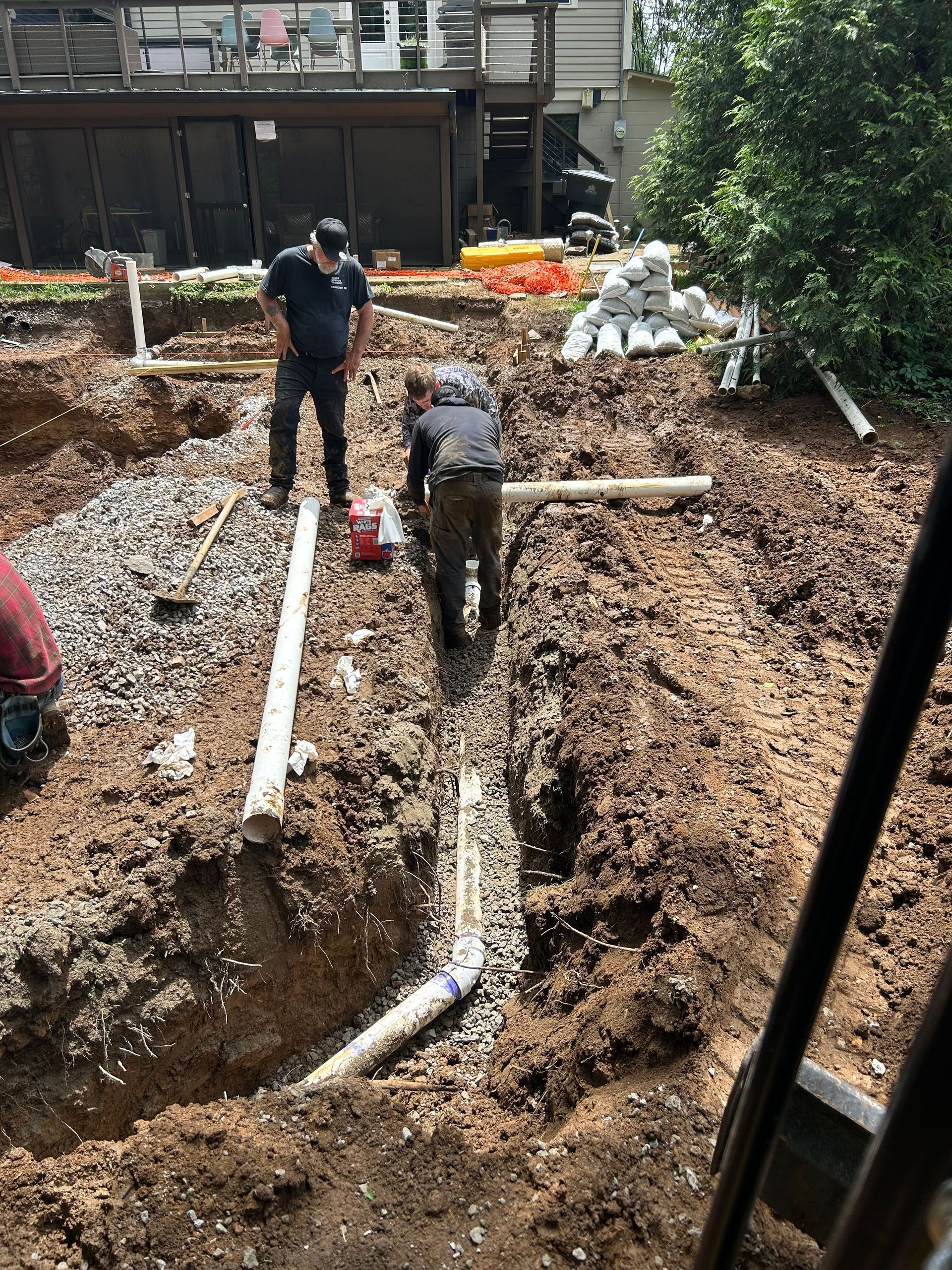 Two people installing drainage pipes in a deep trench at a residential construction site.