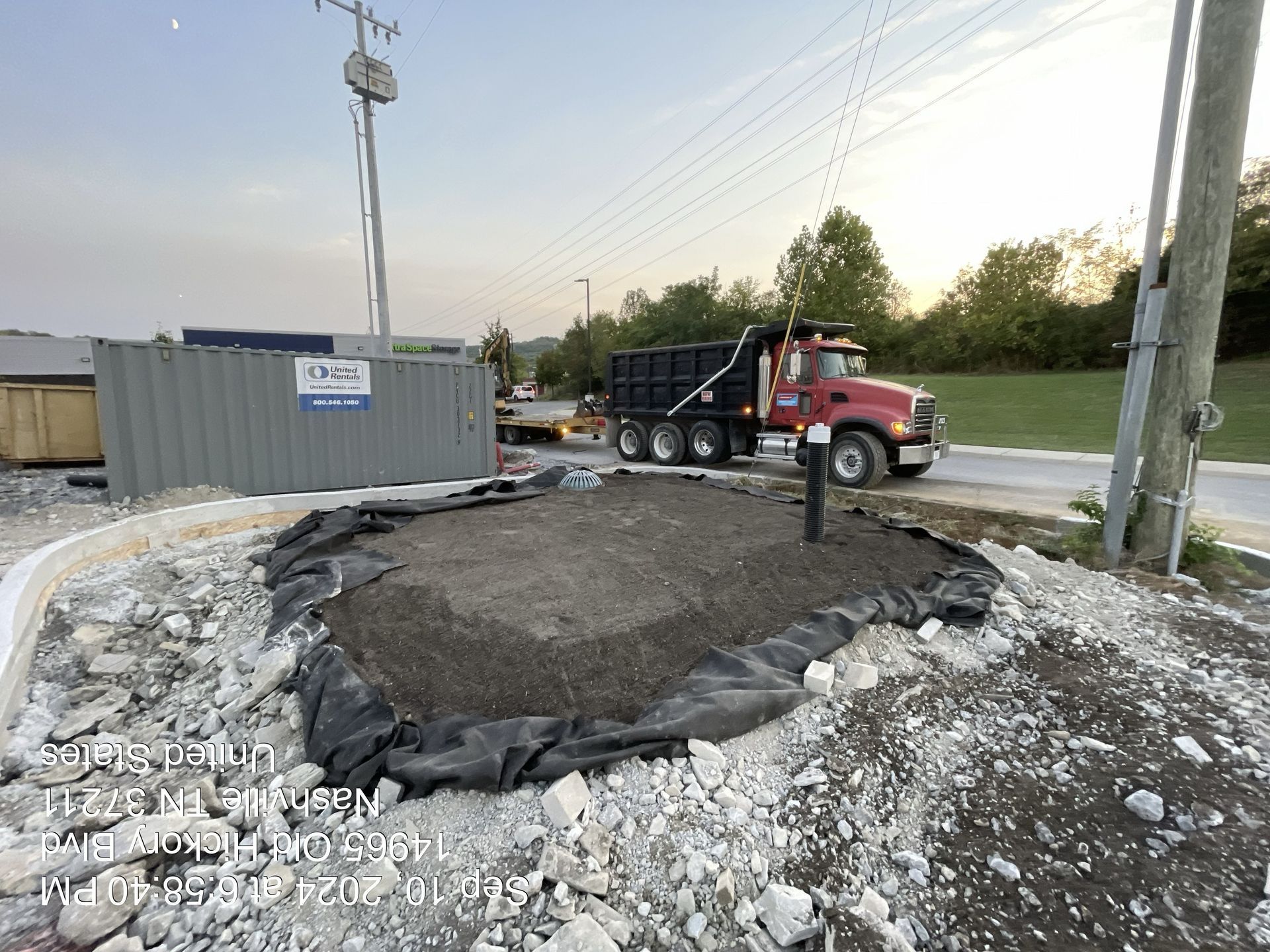 Dump truck unloading gravel beside a construction site near a road at dusk