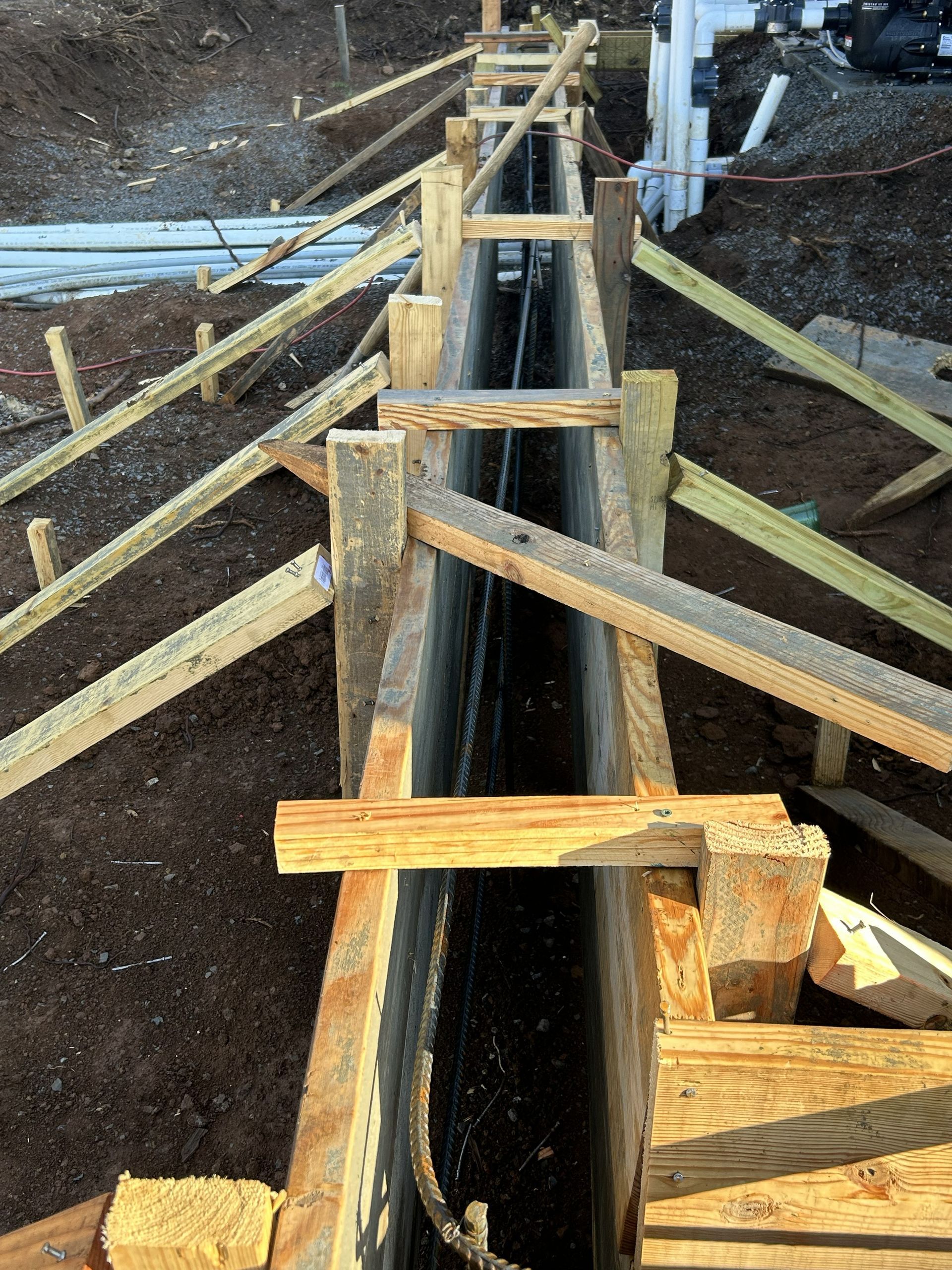 Wooden formwork framing a long concrete trench under construction outdoors