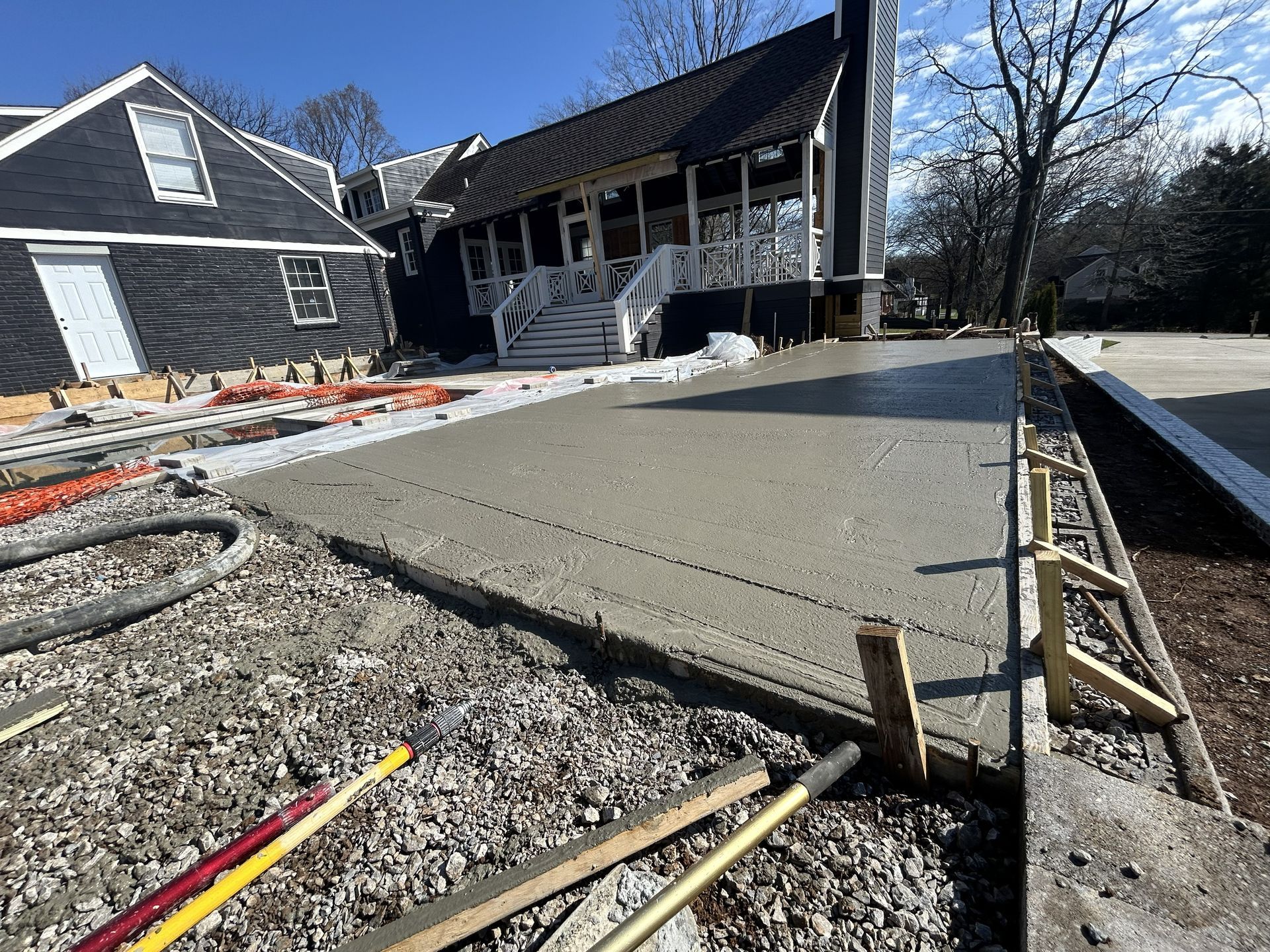Fresh concrete driveway slab beside a house during construction, with wooden forms and tools visible