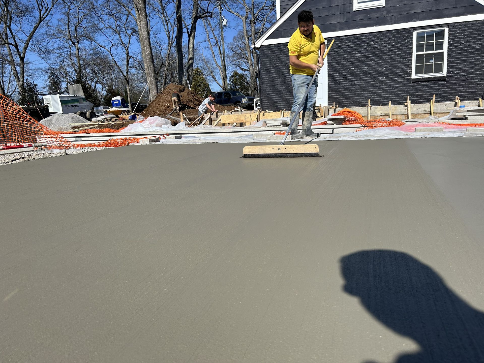 Worker smoothing fresh concrete in a residential driveway with a long-handled tool