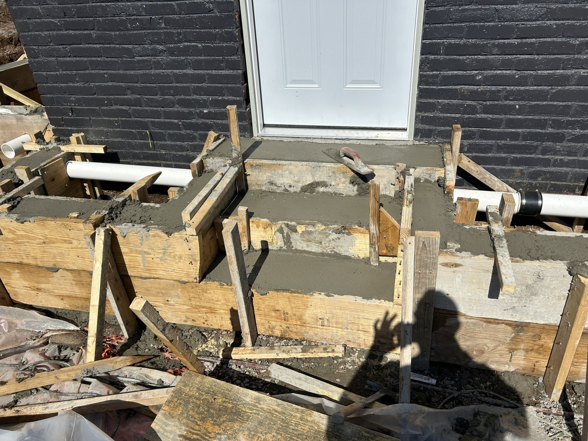 Partially built concrete formwork and rebar in front of a black brick house with a white door