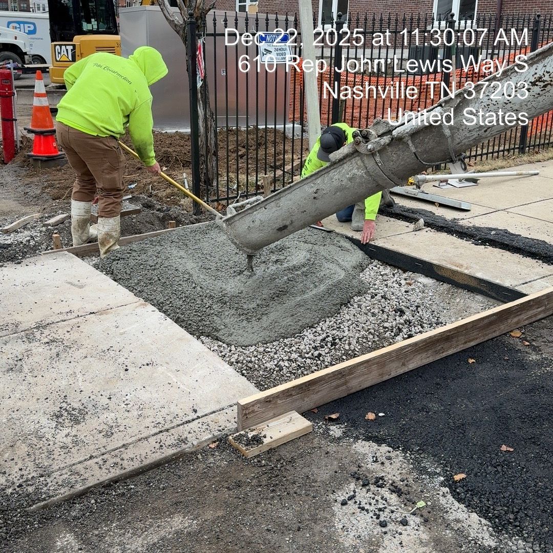 Worker in neon hoodie pouring concrete into a curbside form at a construction site