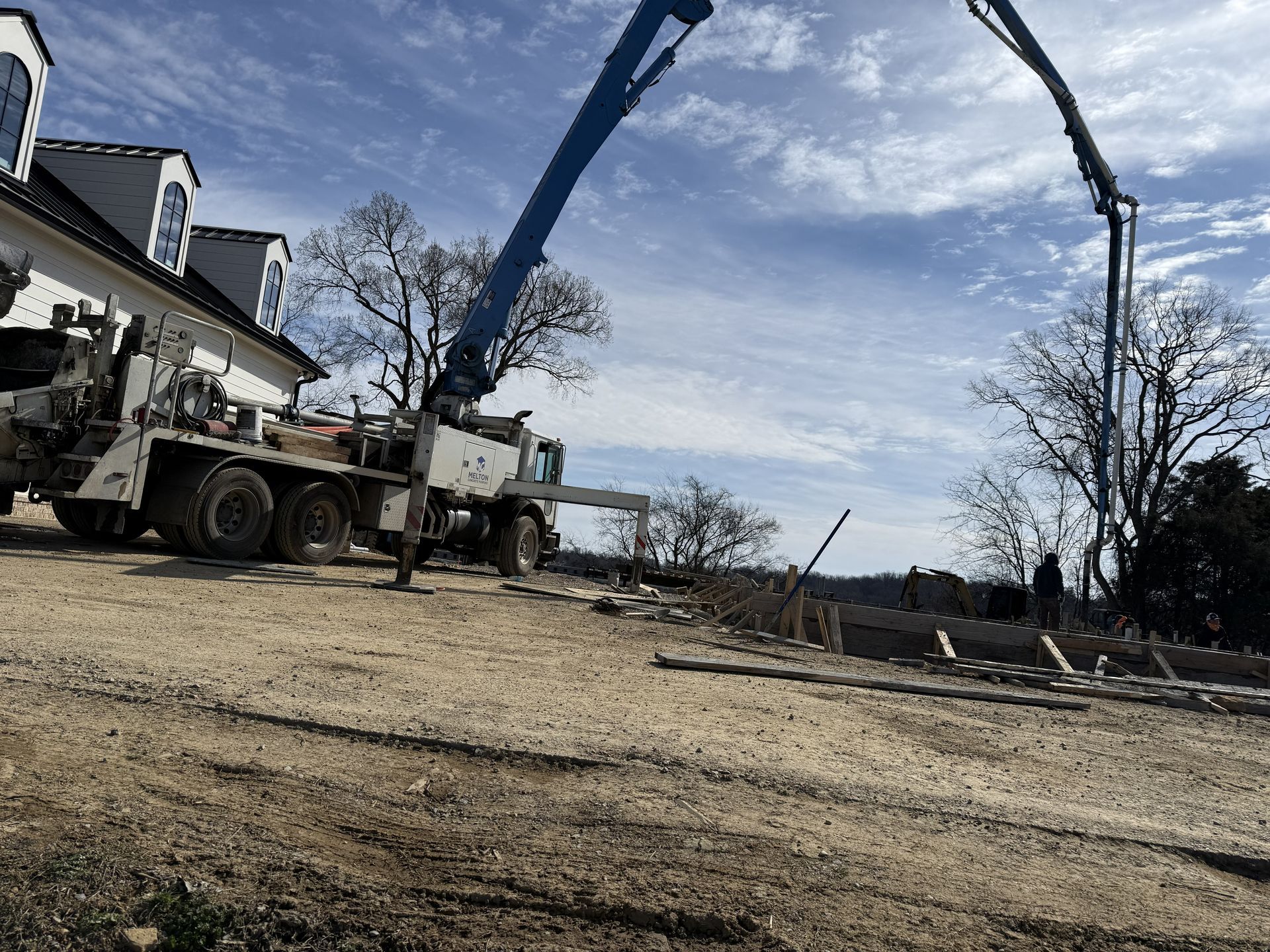 Construction trucks lifting materials beside a house on a partly cloudy day