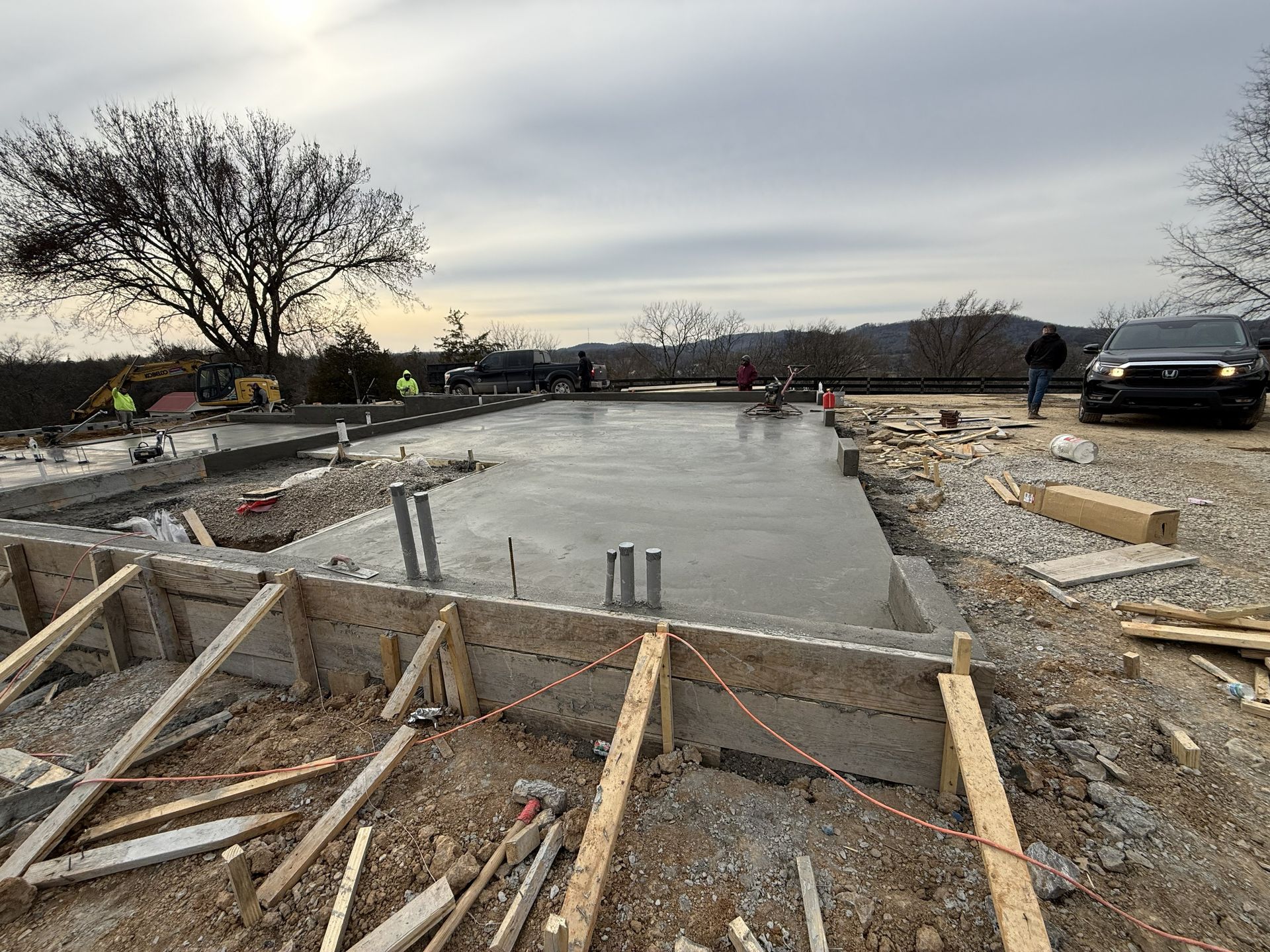Concrete foundation under construction with wooden forms, workers, and a truck at dusk