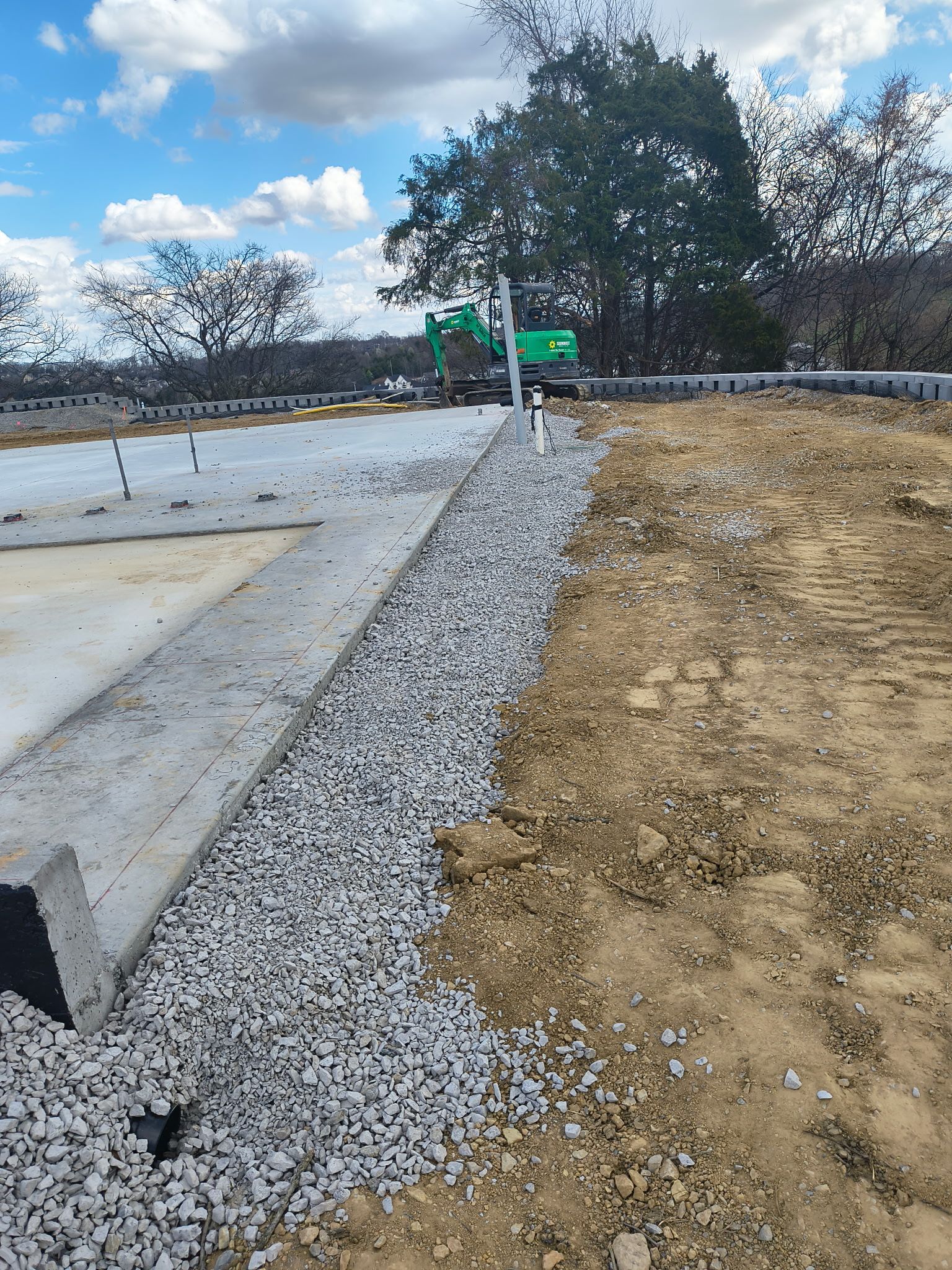 Construction site with concrete pad, gravel edge, and dirt lot under a cloudy sky