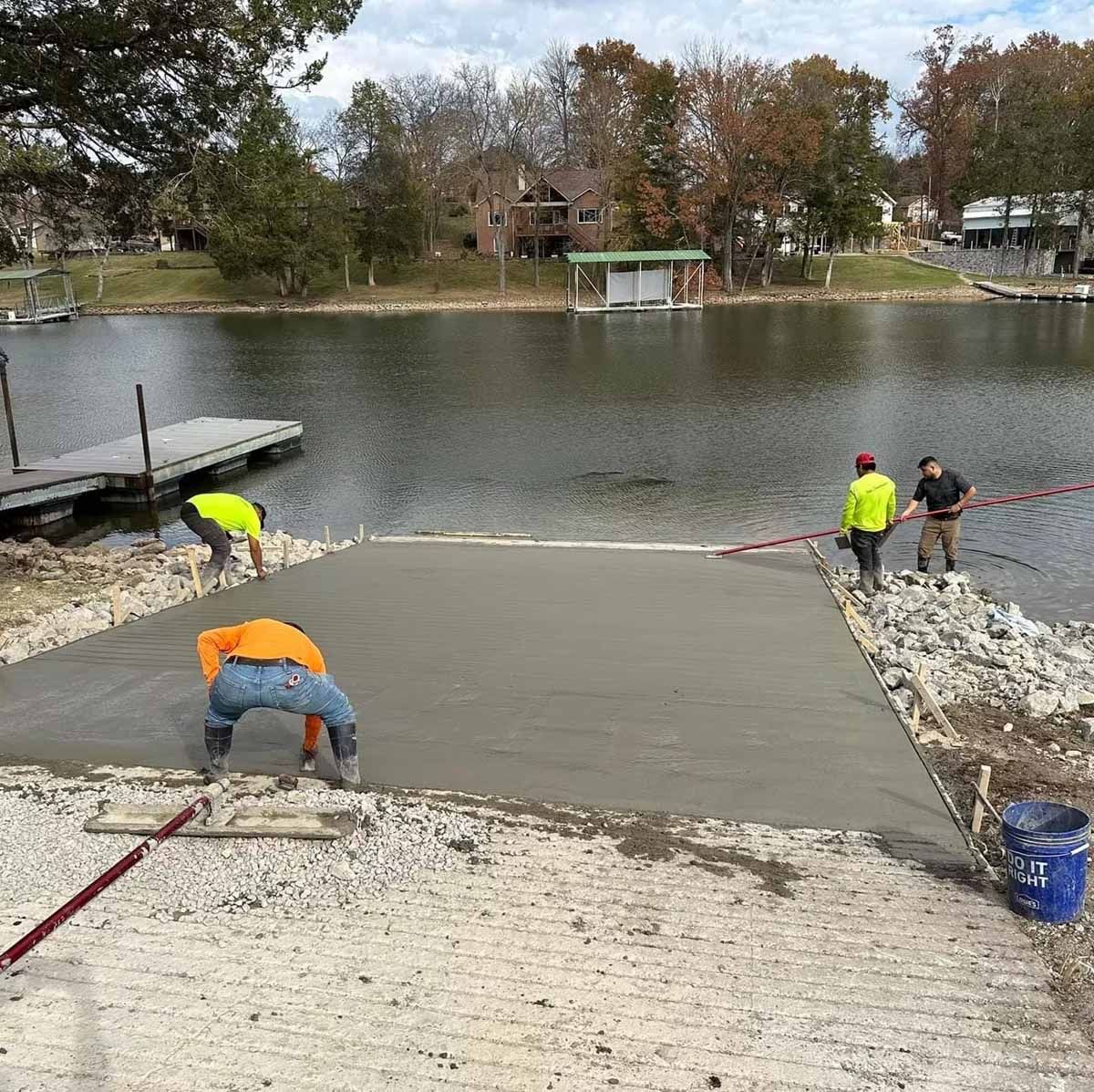 Construction workers pouring concrete for a boat ramp on a lake.