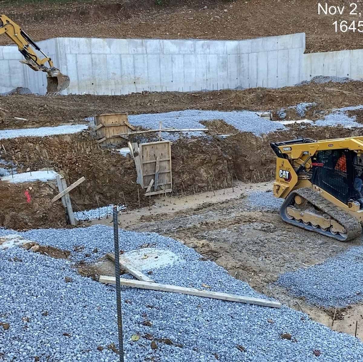 Construction site with heavy machinery, gravel, and a concrete wall.