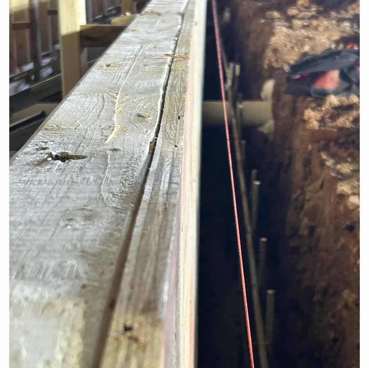 Wooden beam next to a trench with orange string line and metal bars.