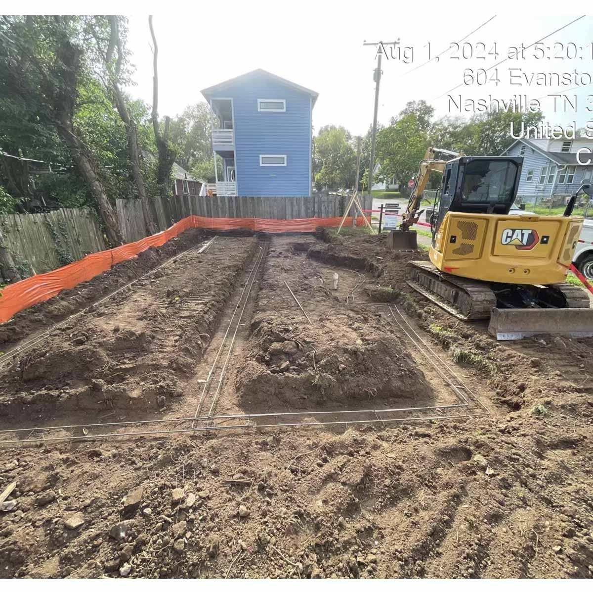 Construction site, Nashville. Yellow excavator, freshly dug dirt with rebar. Orange safety fencing.