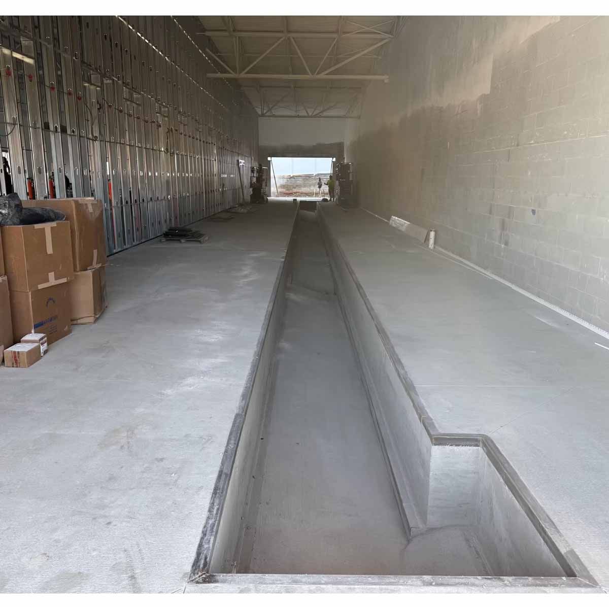 Interior of a concrete building under construction. A long trench runs down the center.