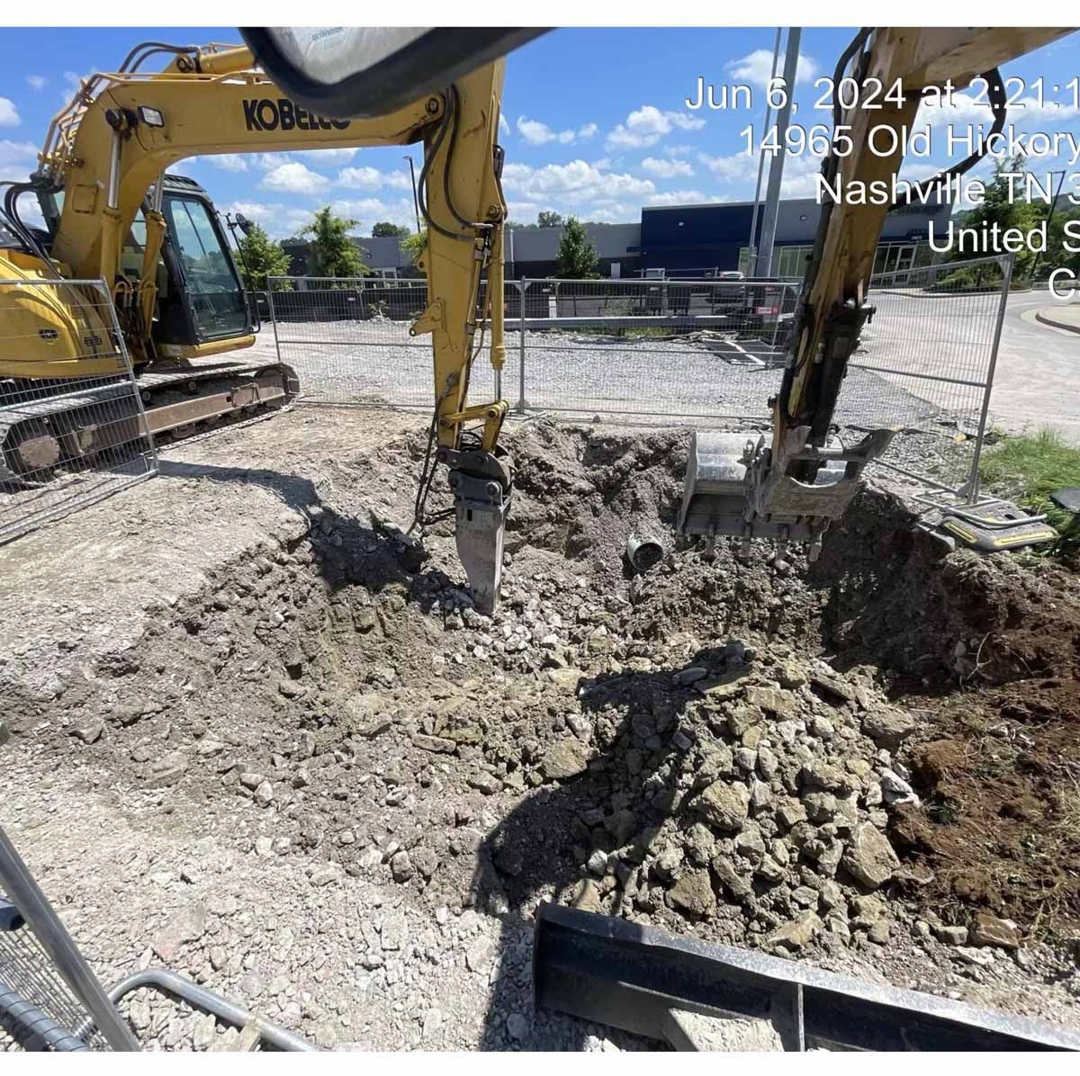 Three yellow excavators on a grassy patch near a small building and trees; some excavation work is underway.