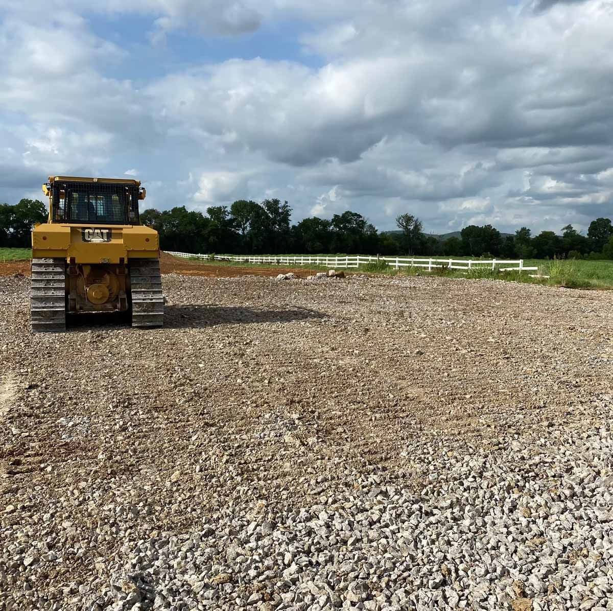 Yellow bulldozer parked on gravel, open field with cloudy sky background.