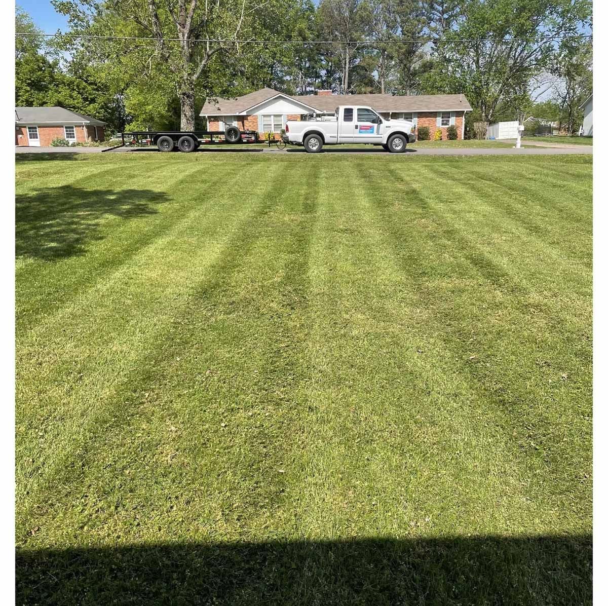 Lawn mowed with stripes. White truck in front of a house. Green grass.