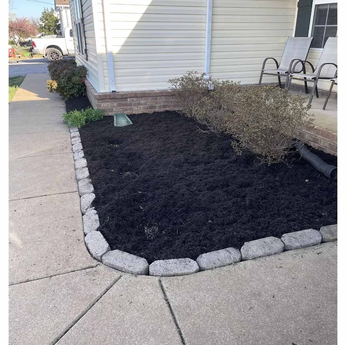 Dark mulch in a raised garden bed bordered by concrete blocks next to a sidewalk and house.