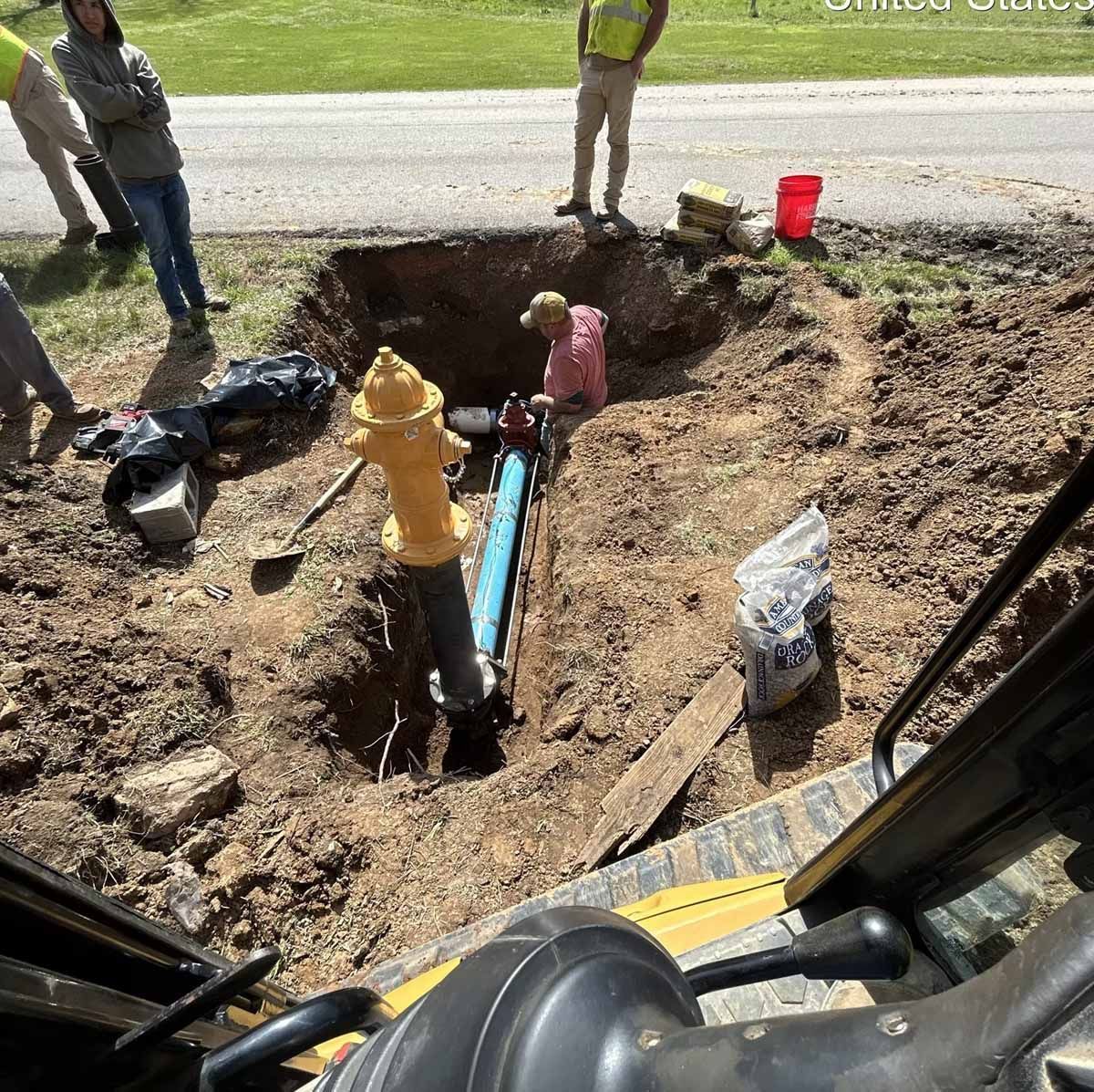 Workers repairing a water main and hydrant in a roadside ditch. The hydrant is yellow.