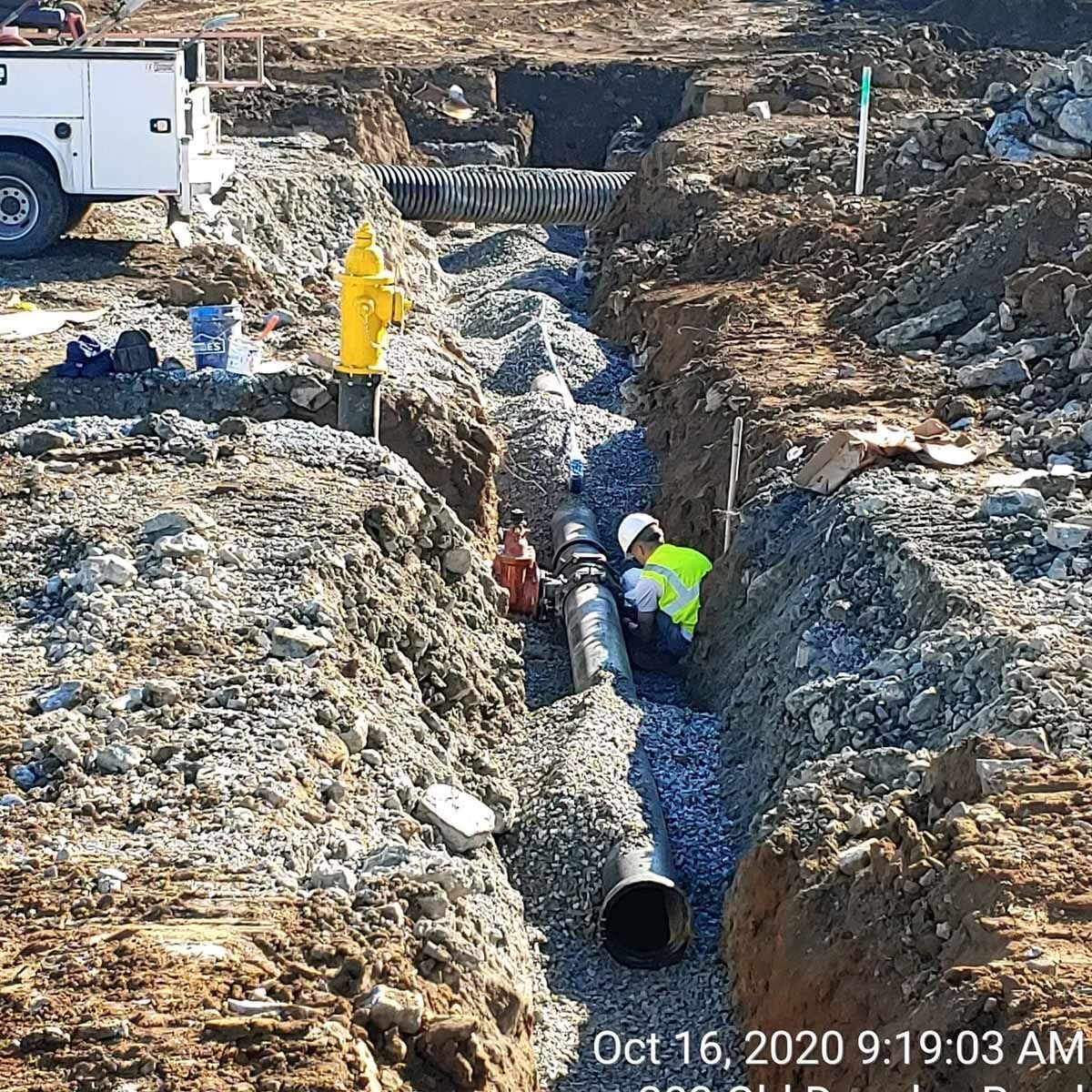 Construction workers installing water pipes in a trench, with gravel base and fire hydrant.