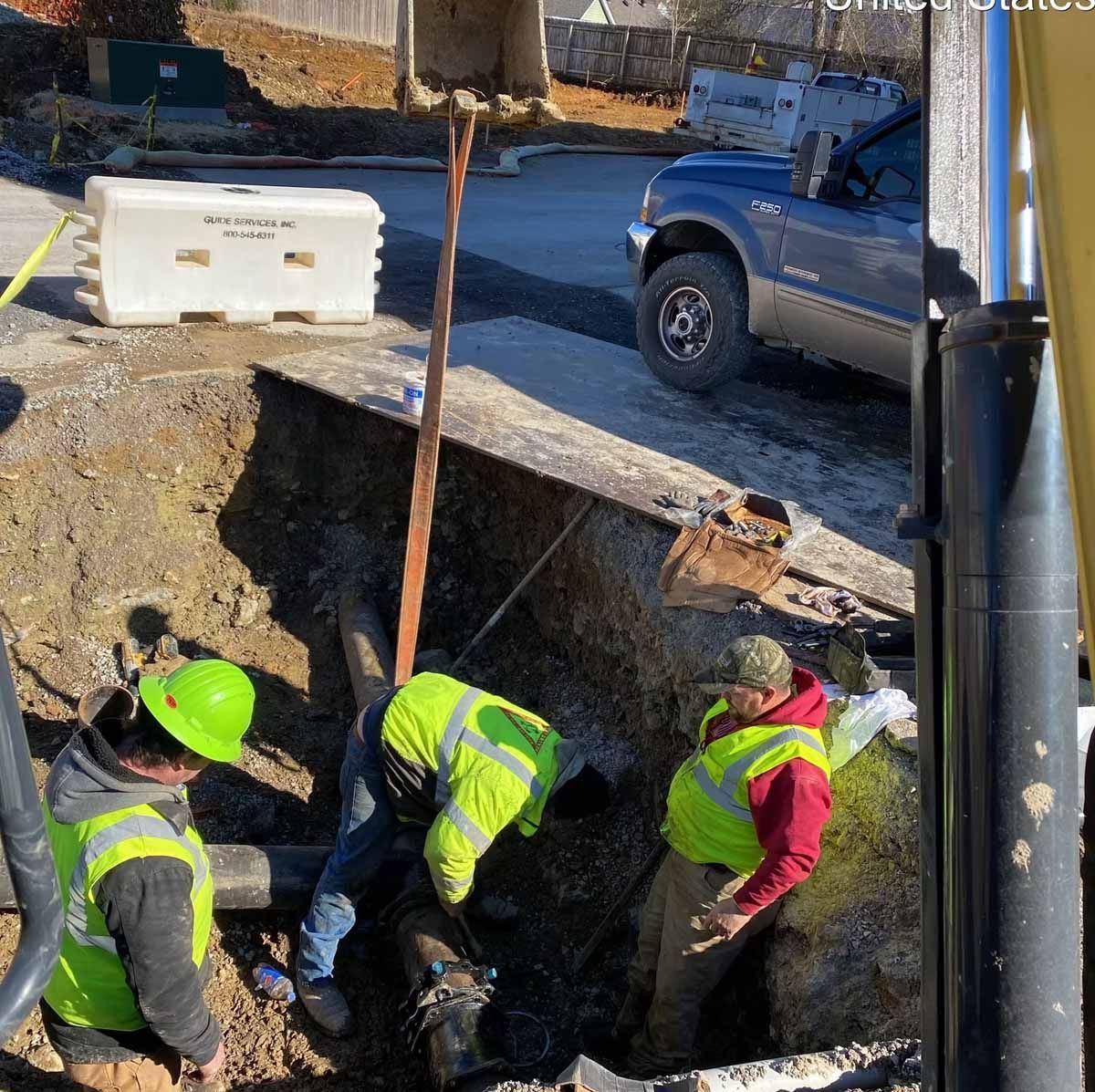 Construction workers in high-visibility vests working on underground pipes in a road trench.