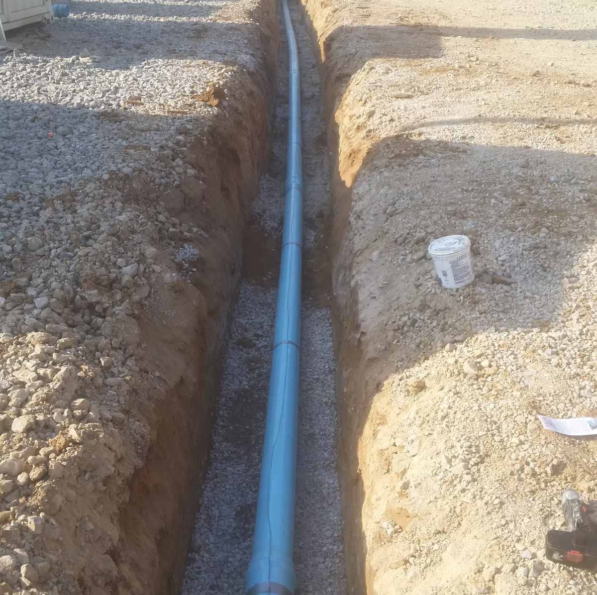 Trench with gray pipe laid in gravel, ready for burial; construction site.