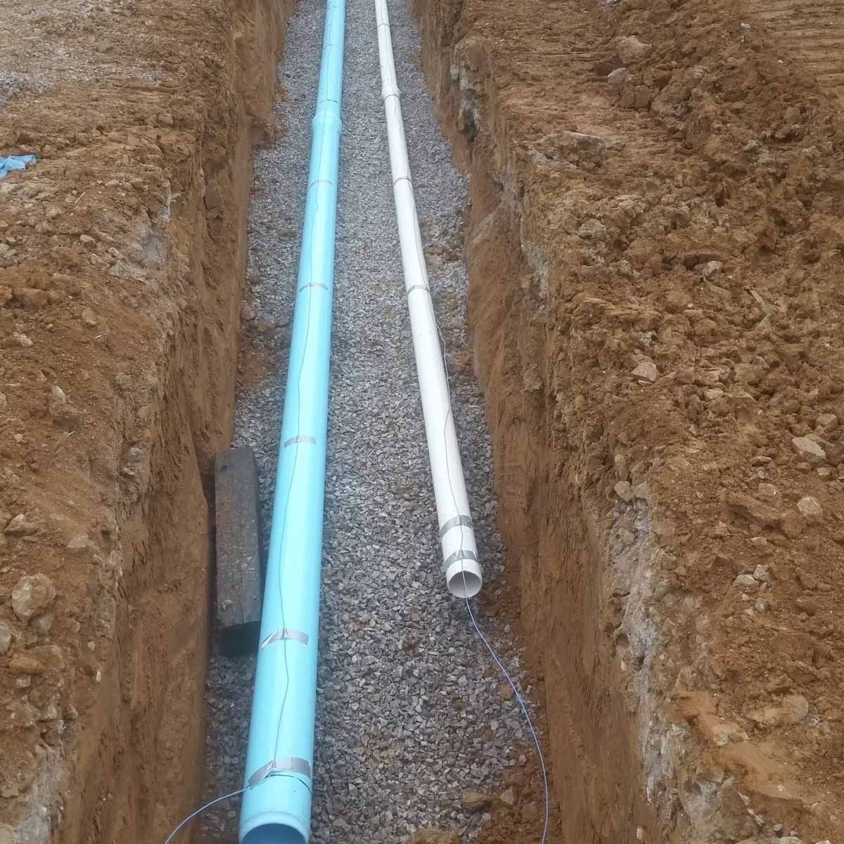 Blue and white pipes laid in a gravel-lined trench, ready for burial.