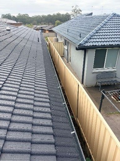 View of two houses with tiled roofs separated by a beige metal fence, seen from above.