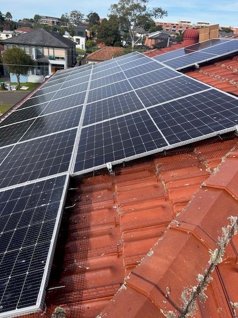 Solar panels installed on a red tile roof of a house in a suburban setting.