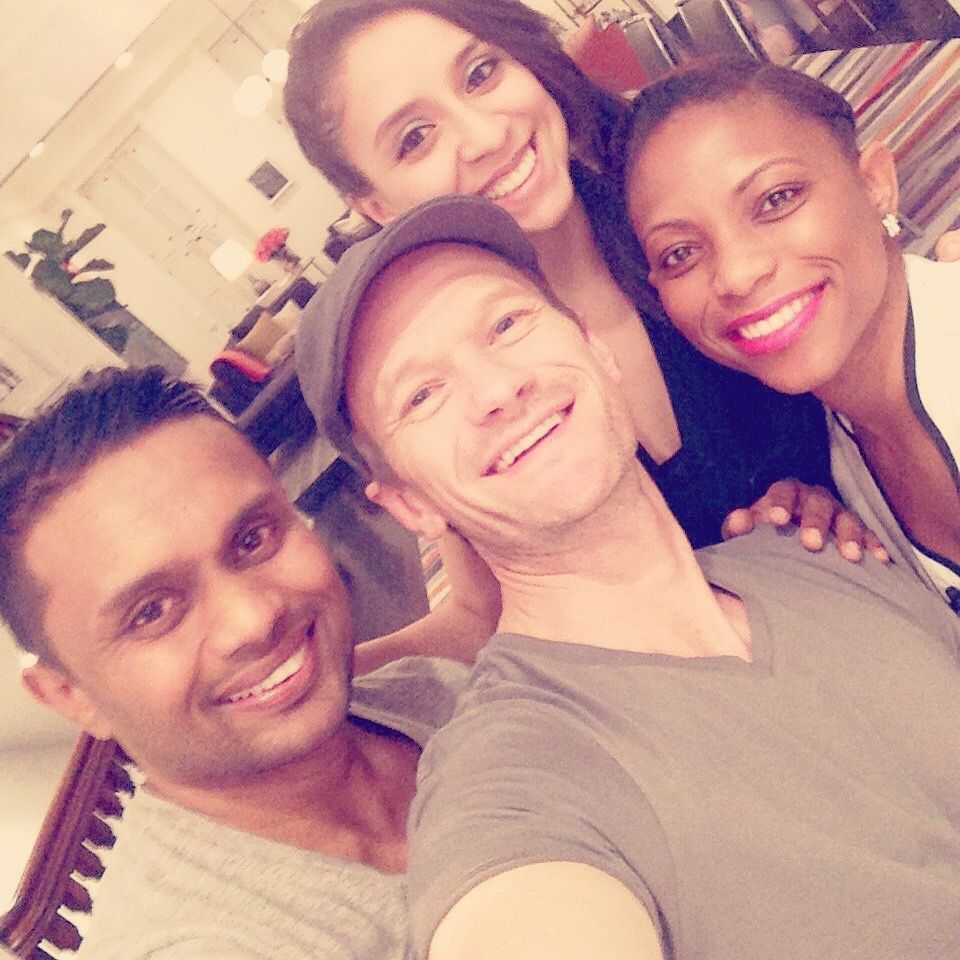 Four smiling people pose for a selfie indoors, one person is wearing a gray cap.