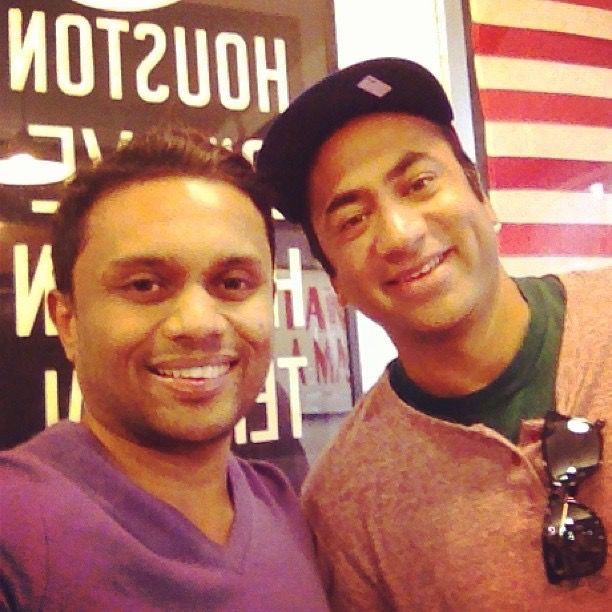 Two men smiling for a selfie in front of a sign that says