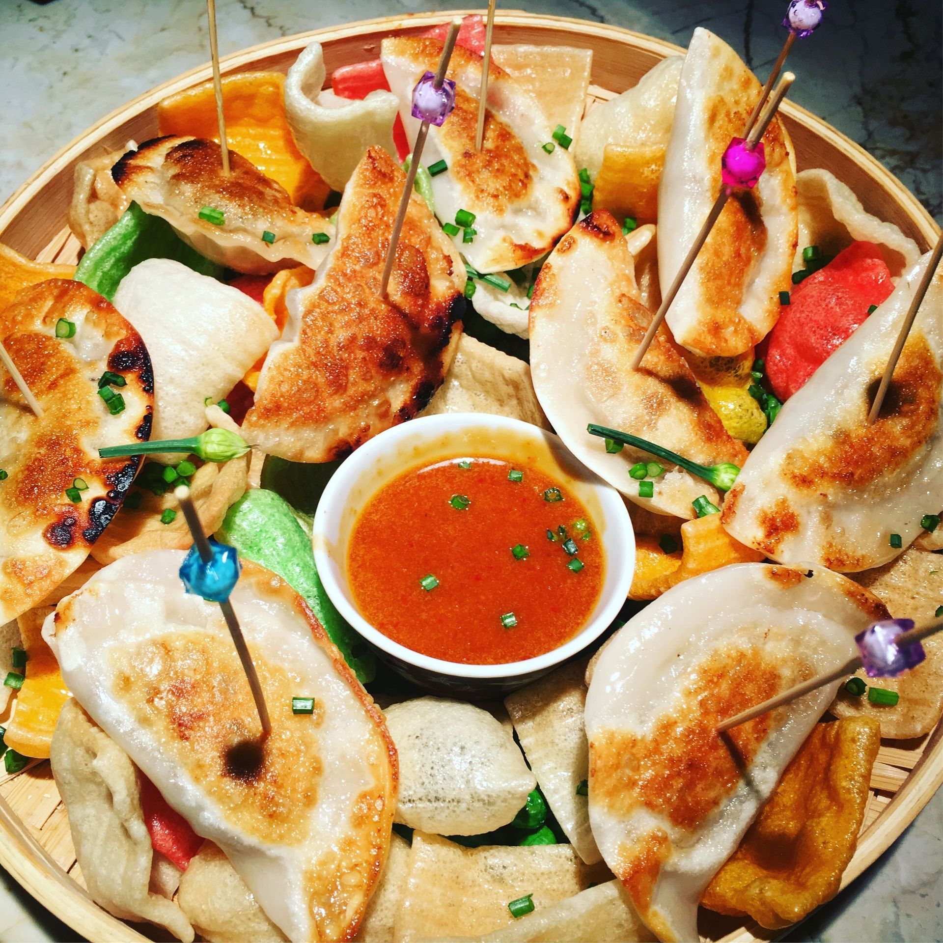 Assorted seafood platter with dipping sauce and colorful toothpicks on a round wooden tray.