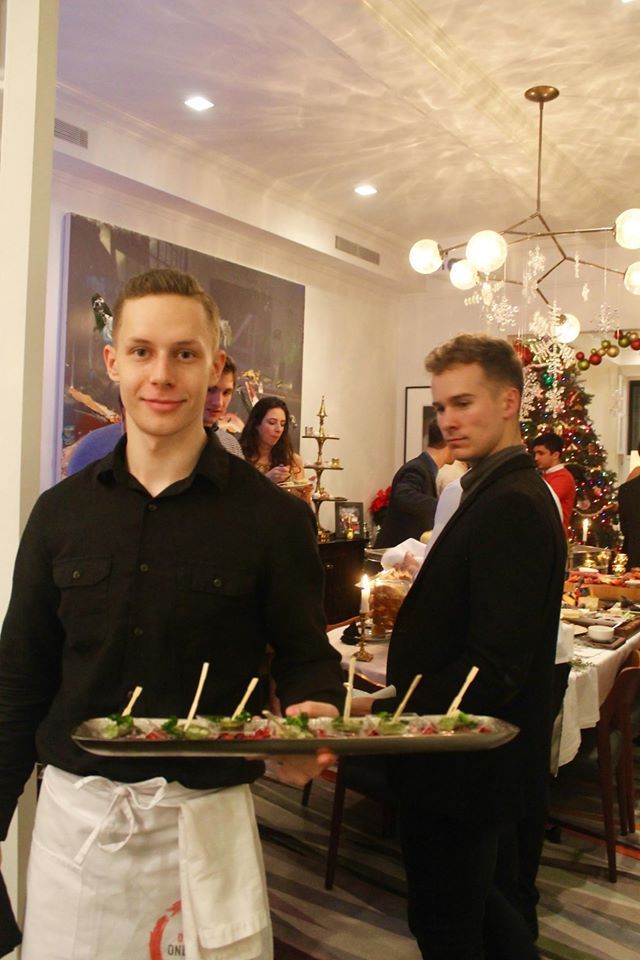 Server holding tray of appetizers, dining room setting, other servers and guests.