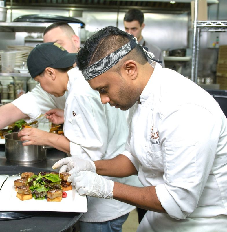 Chefs plating food in a busy kitchen; one chef adds garnish to a dish.