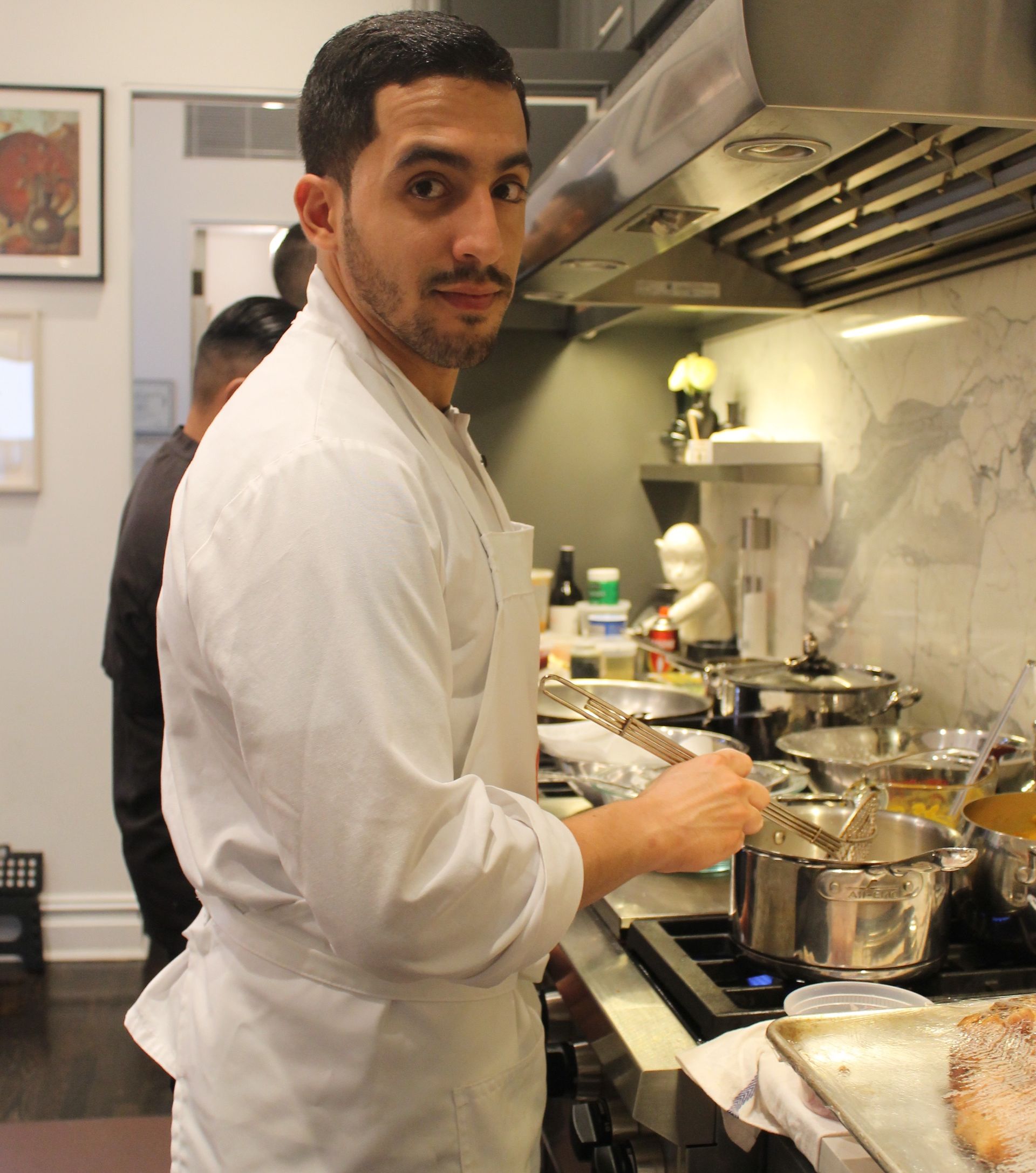 Chef in a white coat cooking in a kitchen, looking at the camera.