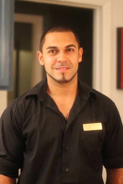 Man in black collared shirt with goatee, smiling. Name tag visible. Interior setting.