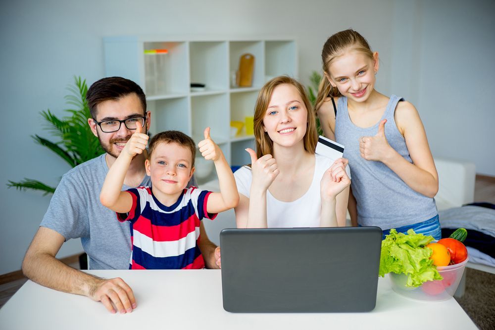 Family of four giving thumbs up while looking at a laptop, holding a credit card.