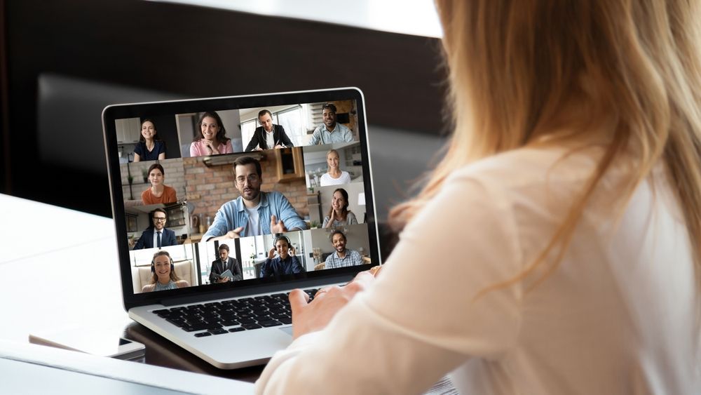 Woman using laptop for a video conference with multiple participants on screen.