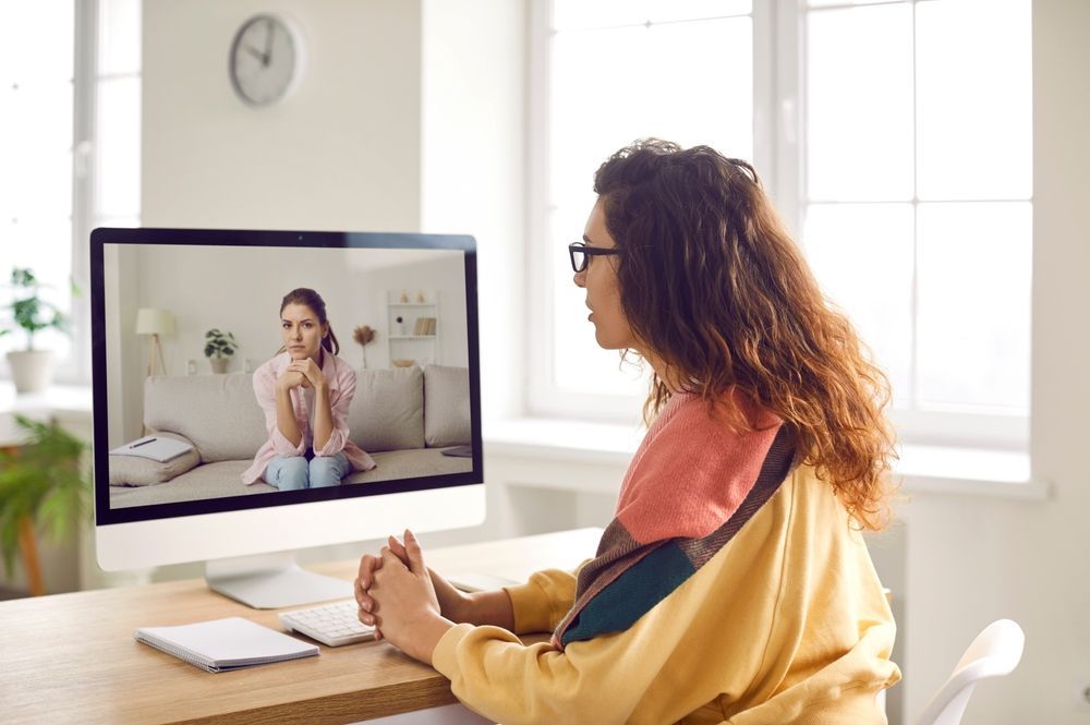 Woman in video call with another woman, looking serious, indoors.