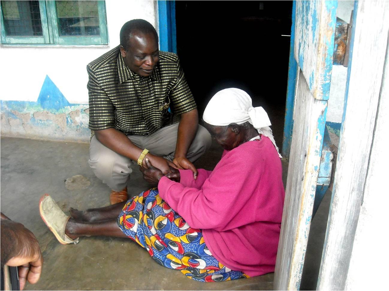 Two people sitting outside a doorway, one helping the other with a foot or hand