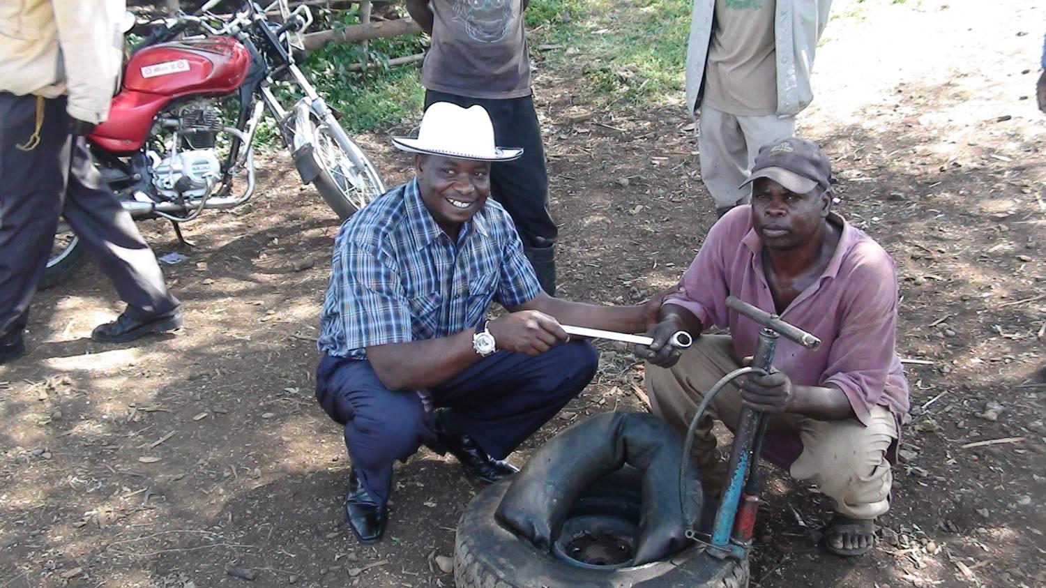 Two men repairing a tire outdoors beside a red motorcycle