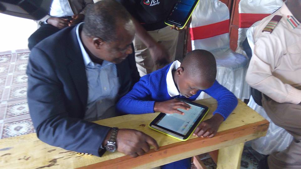 Adult guiding child using a tablet on a wooden bench in a classroom setting