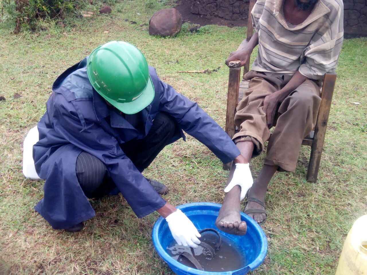 Two people in work gear kneel by a blue basin, washing a muddy object outdoors.