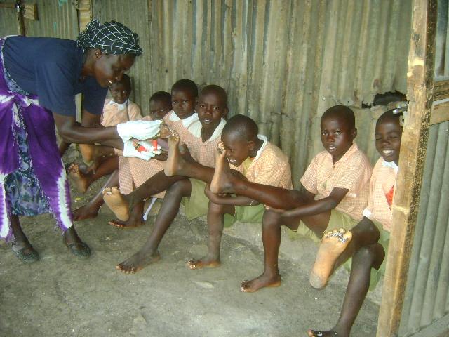 Woman helping seated children in a rustic classroom, one child holding a paper roll
