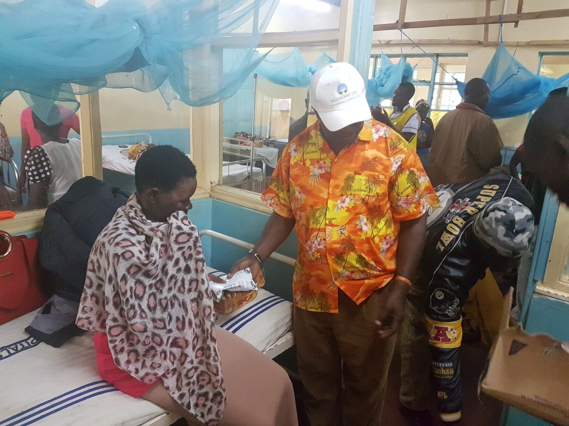 Masked health worker checking a seated patient in a clinic with blue drapes and other people nearby