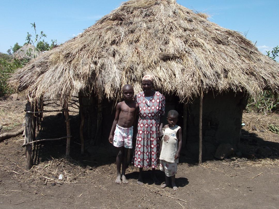 Three people standing in front of a thatched hut under a clear sky
