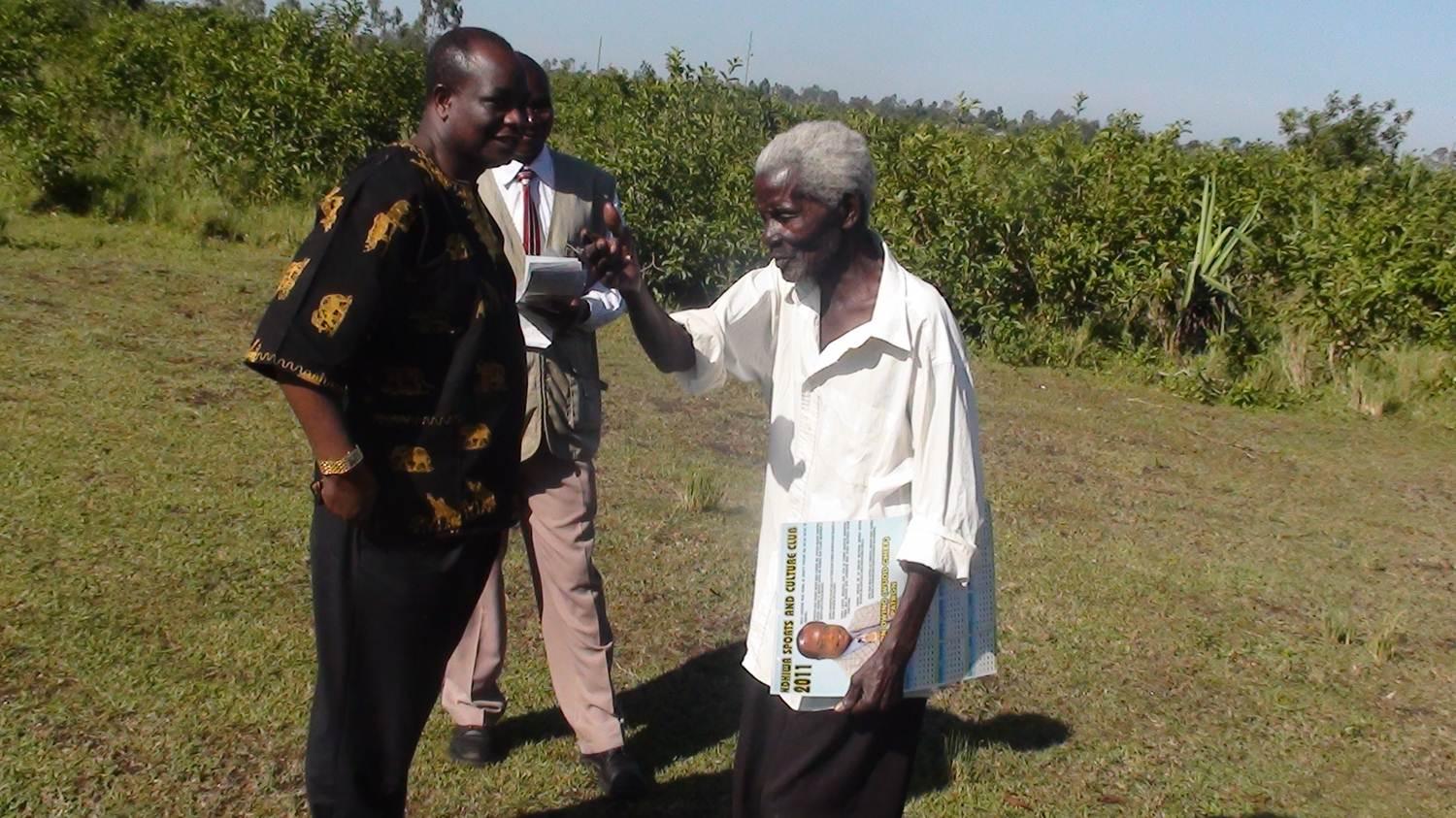 Three people standing and talking in a grassy field under bright sunlight