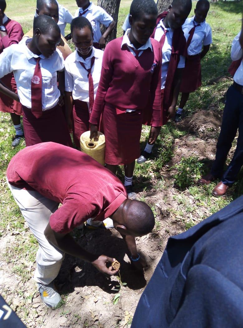 Students in maroon uniforms gather outdoors while one bends to inspect something on the ground.