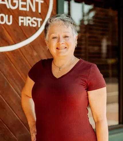 Woman with short gray hair in a maroon shirt, smiling, standing outside a building.