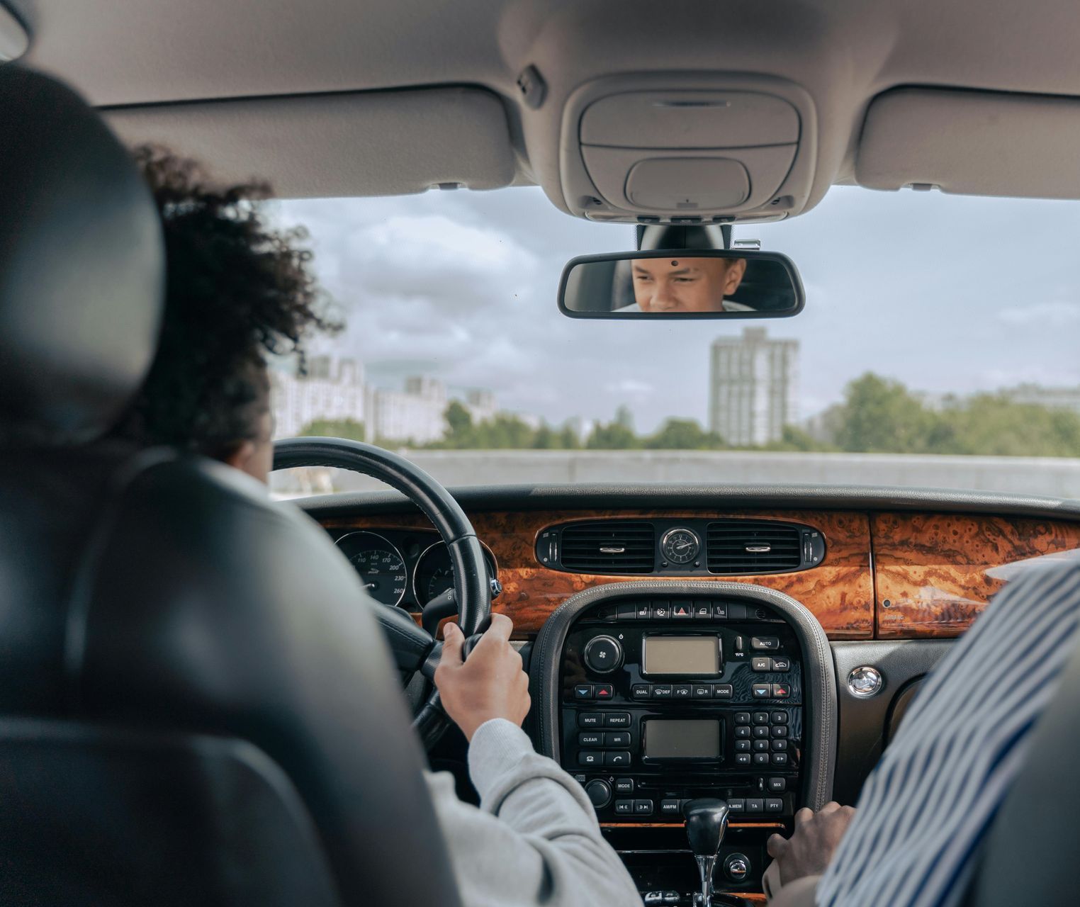 Person driving a car with a passenger; visible in rearview mirror and dashboard details.