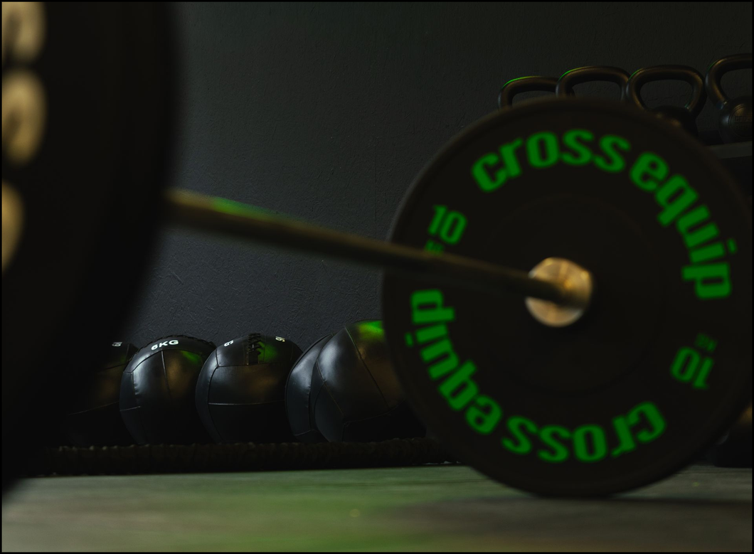 Black dumbbells on a gym floor, with a blurred green cross-training weight plate in the background