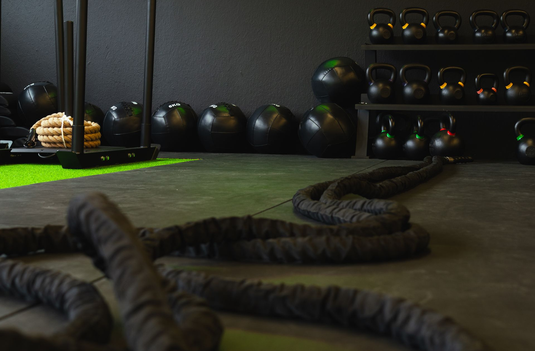 Indoor gym with battle ropes, medicine balls, and shelves of kettlebells on a turf floor